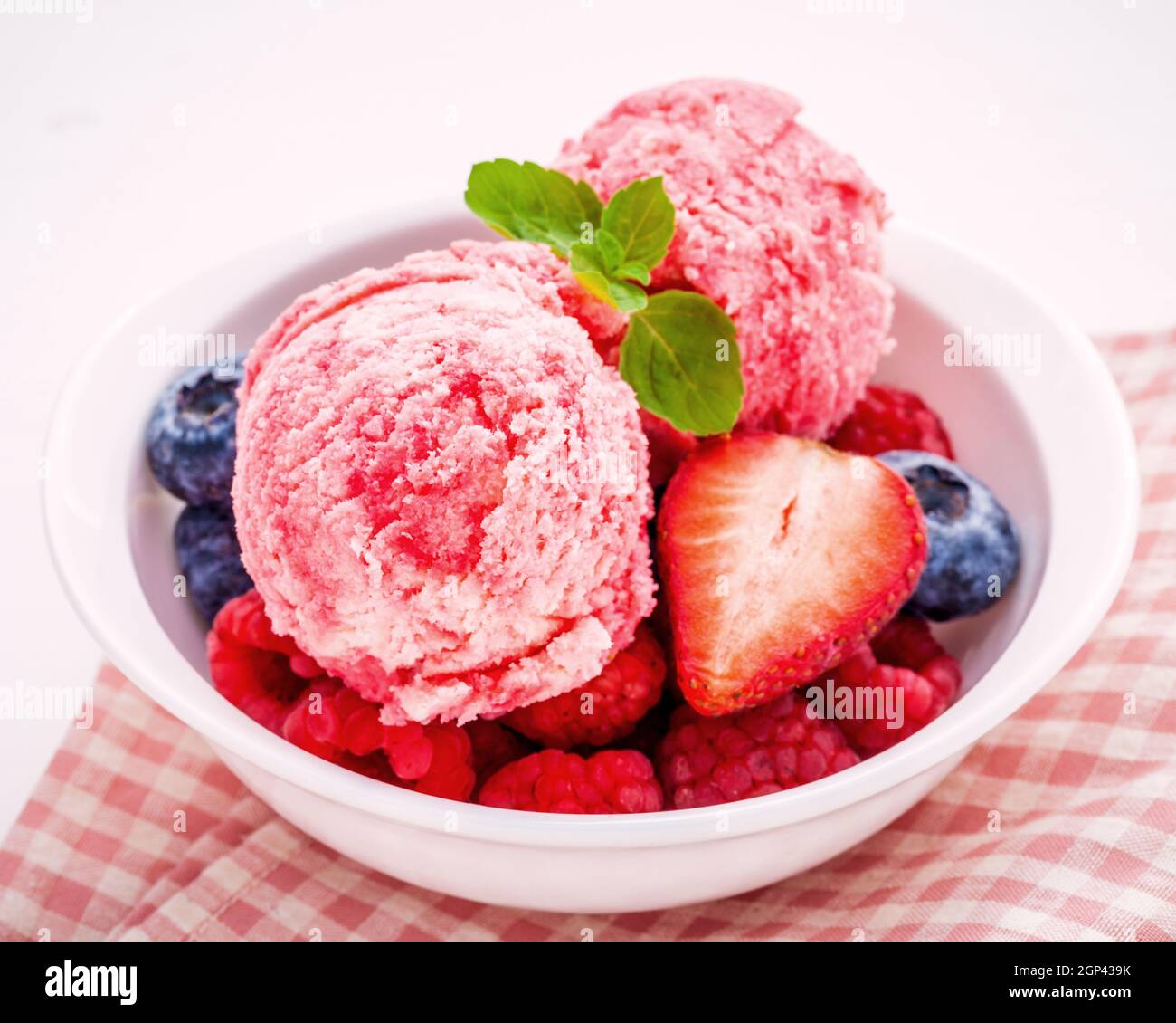 Close up gelato di frutti di bosco misti di frutta Lampone ,mirtillo ,fragola e foglie di menta piperita setup nella ciotola bianco su bianco sullo sfondo di legno . Estate un Foto Stock