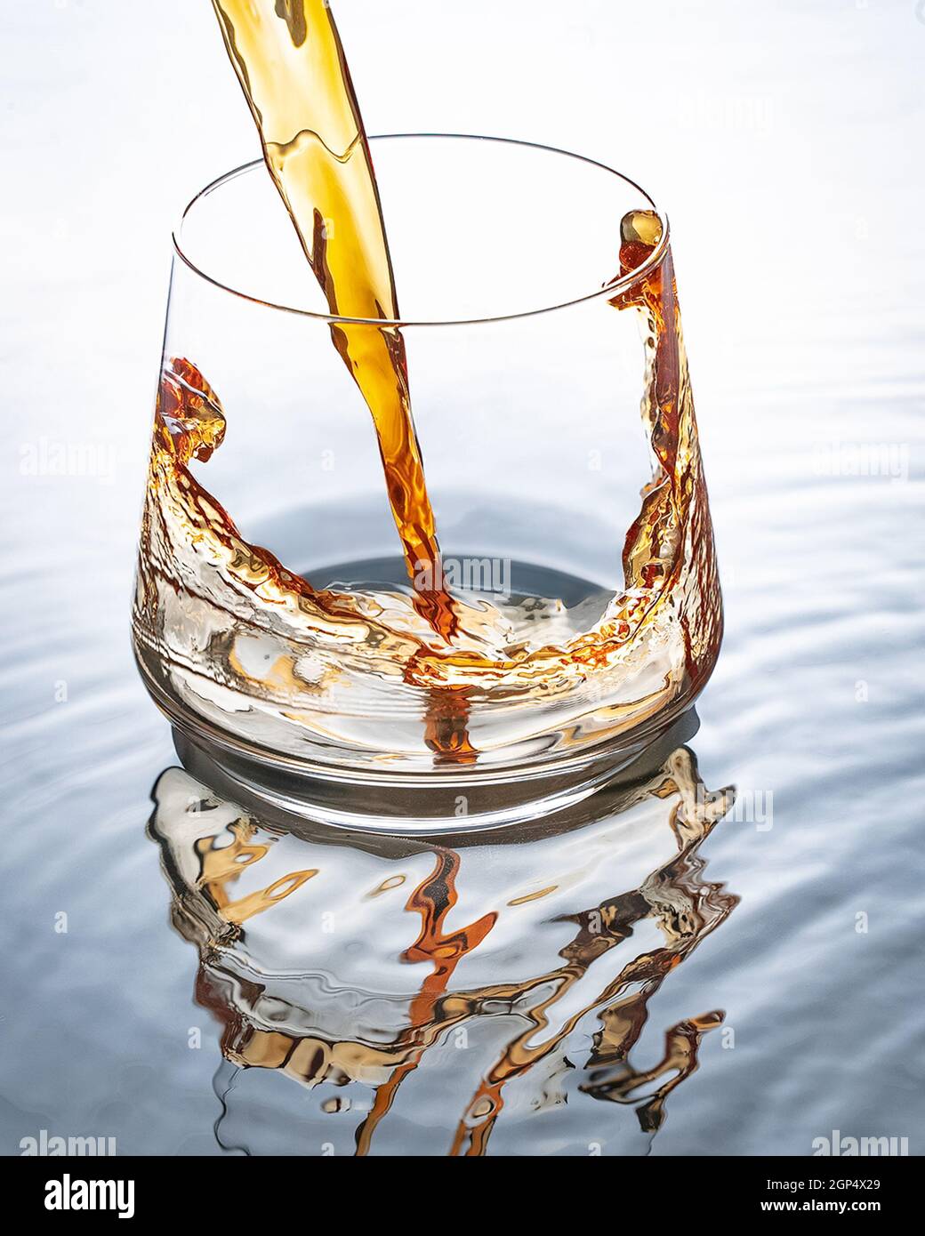 In un bicchiere versare il whiskey. Vetro sullo sfondo di bianco e acqua. Foto Stock