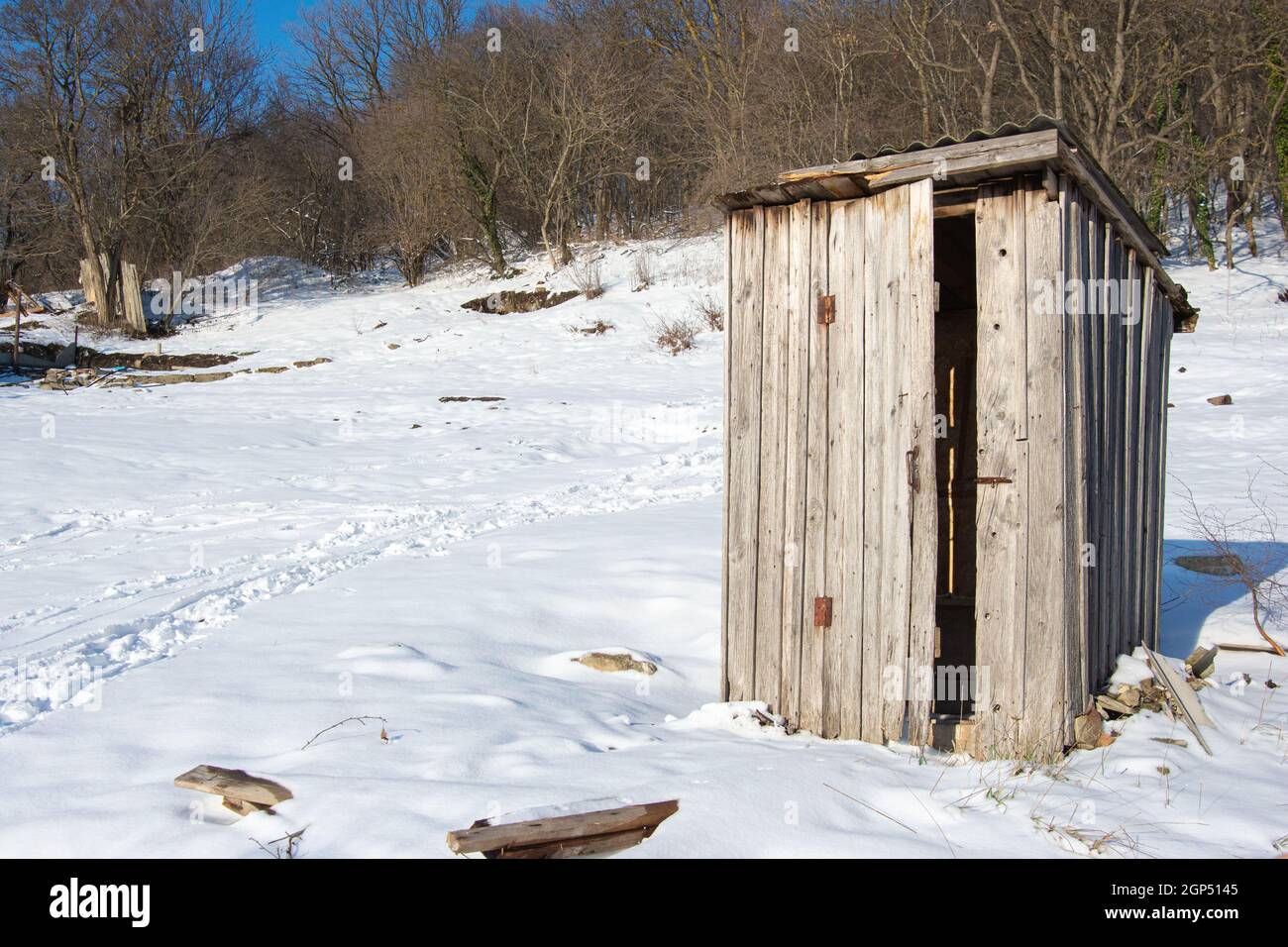 Un vecchio gabinetto di legno si erge da solo su un vuoto terreno coperto di neve Foto Stock