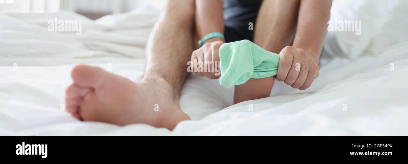 L'uomo mette la calza turchese sulla gamba mentre si siede sul letto Foto Stock
