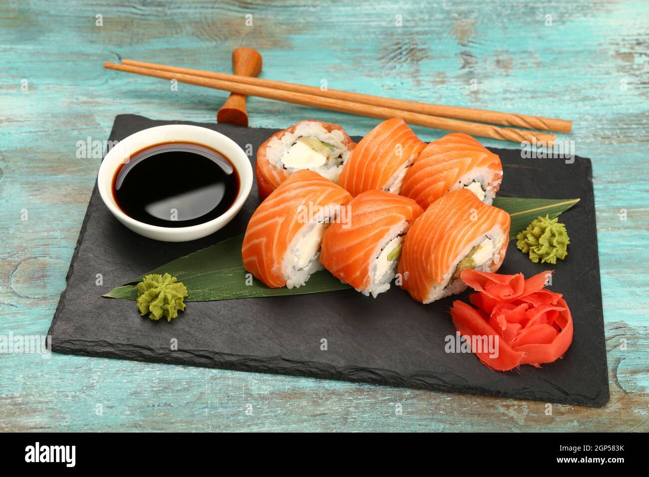 Set da primo piano di sei panini di sushi Filadelfia con salmone crudo servito sulla tavola di ardesia nera su un tavolo blu, vista ad angolo alto Foto Stock