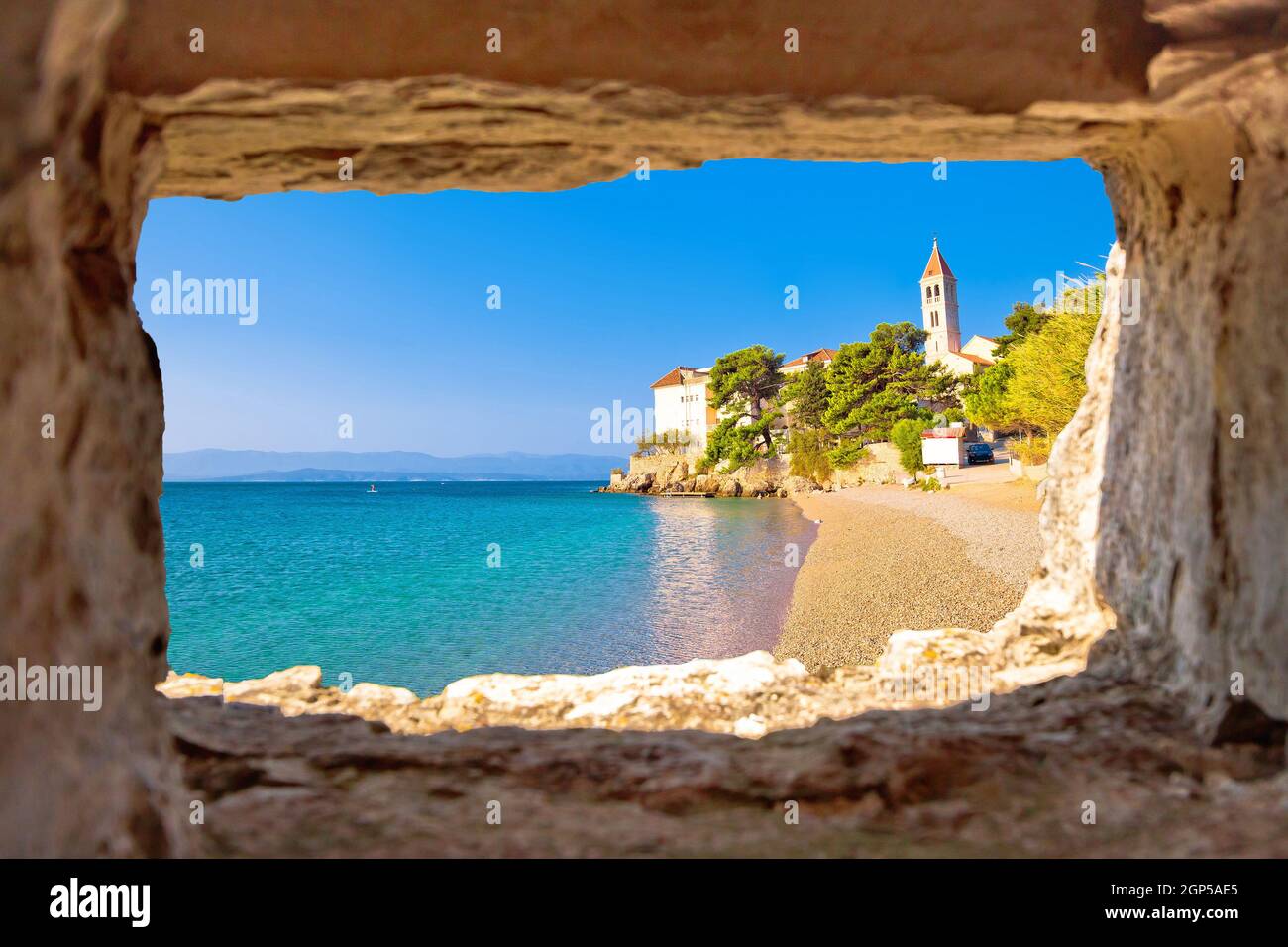 Monastero sulla spiaggia di ciottoli a Bol vista attraverso la finestra di pietra, isola di Brac, Dalmazia, Croazia Foto Stock