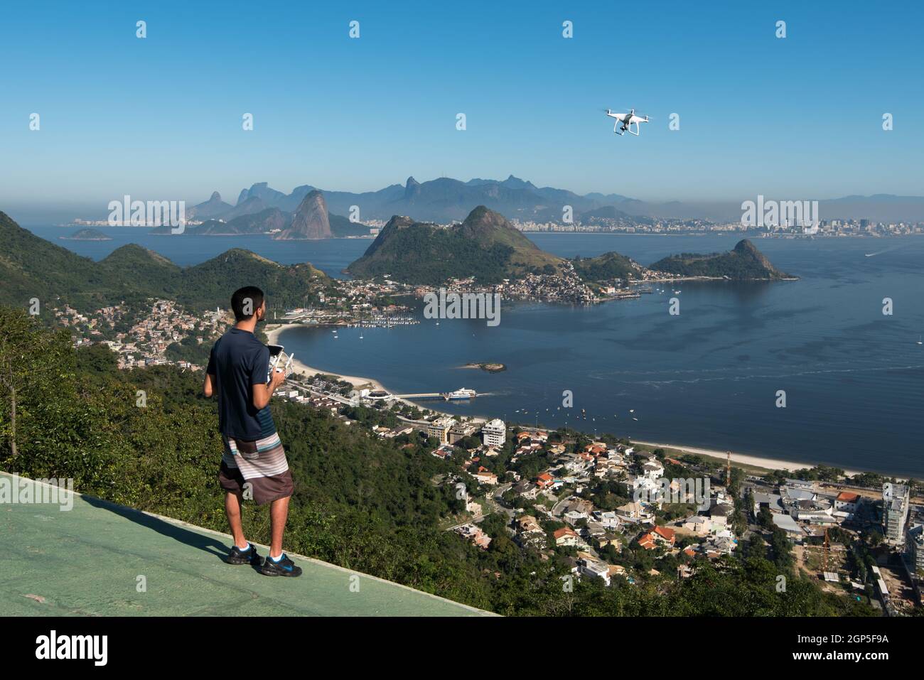 Nitreoi, RJ, Brasile - 5 luglio 2016: Giovane che controlla un drone in un parco con una bella vista della città di Rio de Janeiro. Foto Stock