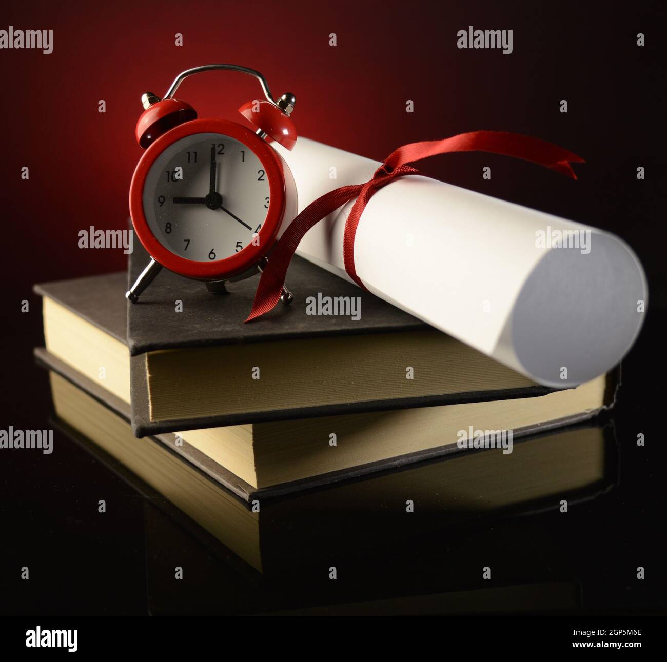 Un diploma in cima a una coppia di libri mostra il successo di profitto degli studi scolastici, mentre un orologio sveglia ci ricorda l'importante calendario a portata di mano. Foto Stock