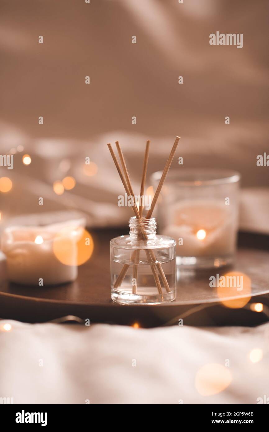 Profumo domestico in bottiglia di vetro con i bastoni di legno, vassoio profumato delle candele di combustione in camera da letto vicino. Aromaterapia atmosfera accogliente stile di vita. Inverno caldo xma Foto Stock
