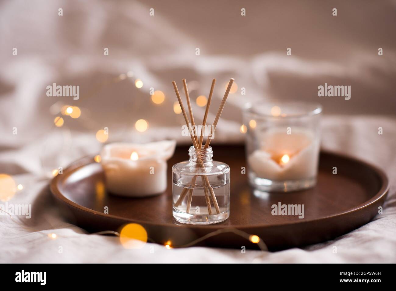 Profumo domestico in bottiglia di vetro con i bastoni di legno, vassoio profumato delle candele di combustione in camera da letto vicino. Aromaterapia atmosfera accogliente stile di vita. Inverno caldo xma Foto Stock