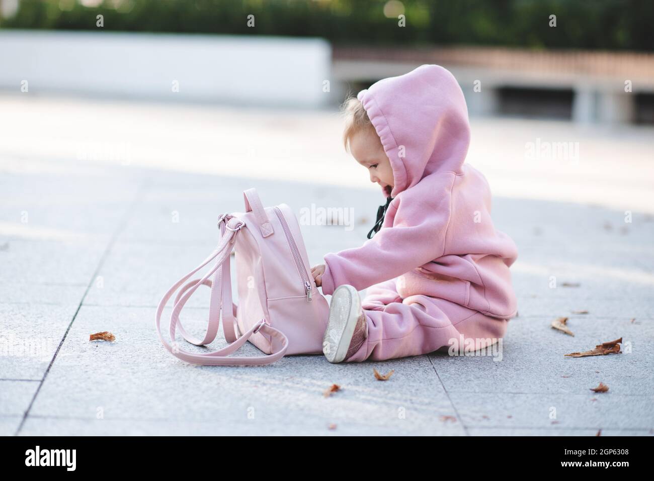 Divertente bambina 1 anno di età indossare elegante tuta rosa sport e zaino  seduta su strada su sfondo urbano. Bambino piccolo carino con c trendy Foto  stock - Alamy