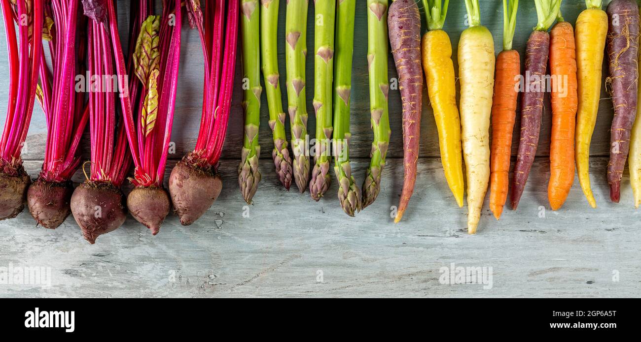 Varie verdure di radice su sfondo di legno. Ravanelli, carote colorate e asparagi. Foto Stock