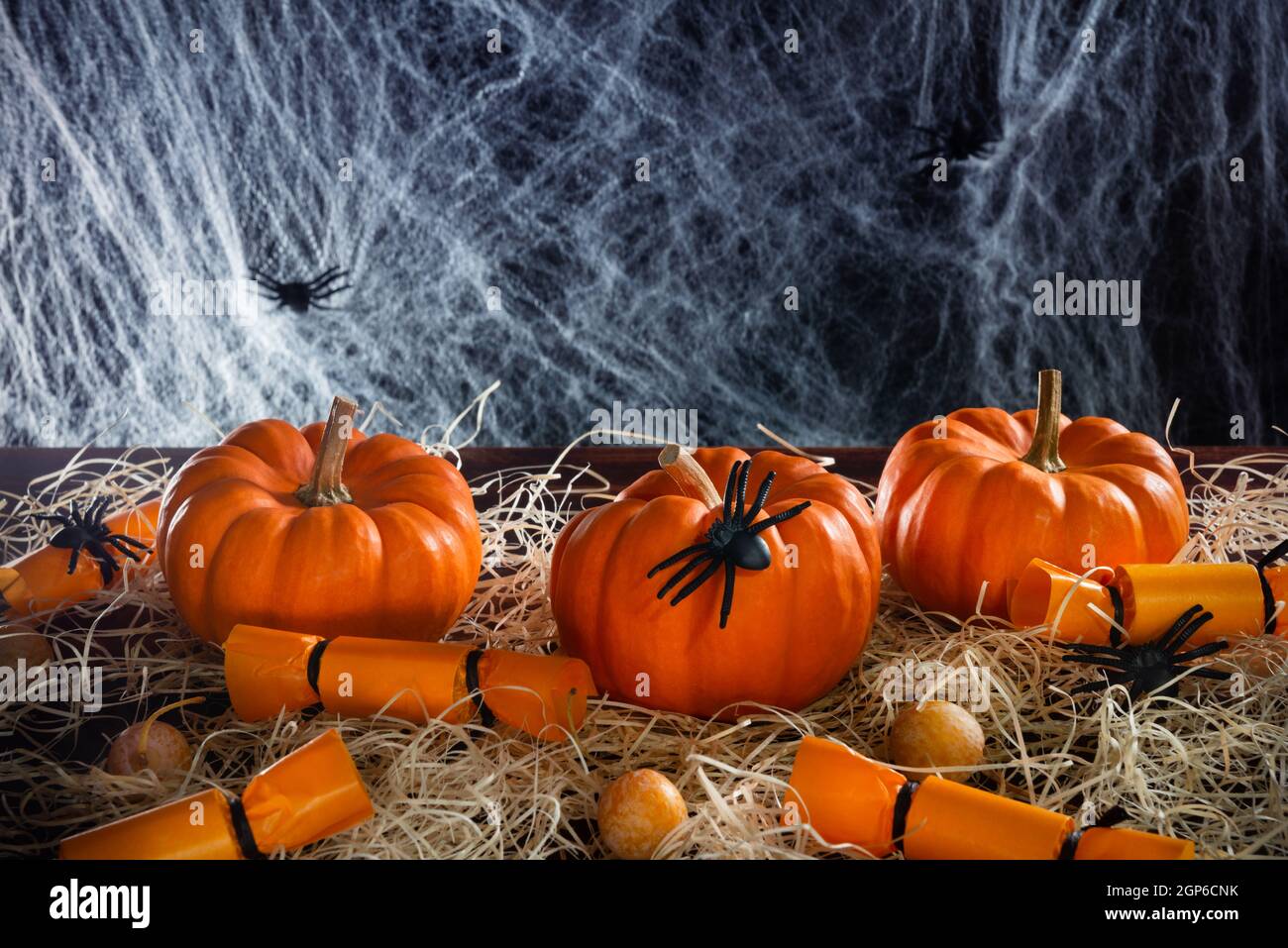 Zucche, caramelle, ragni e rete di ragno decorata paglia su sfondo nero, concetto di festa di Halloween, spazio copia Foto Stock