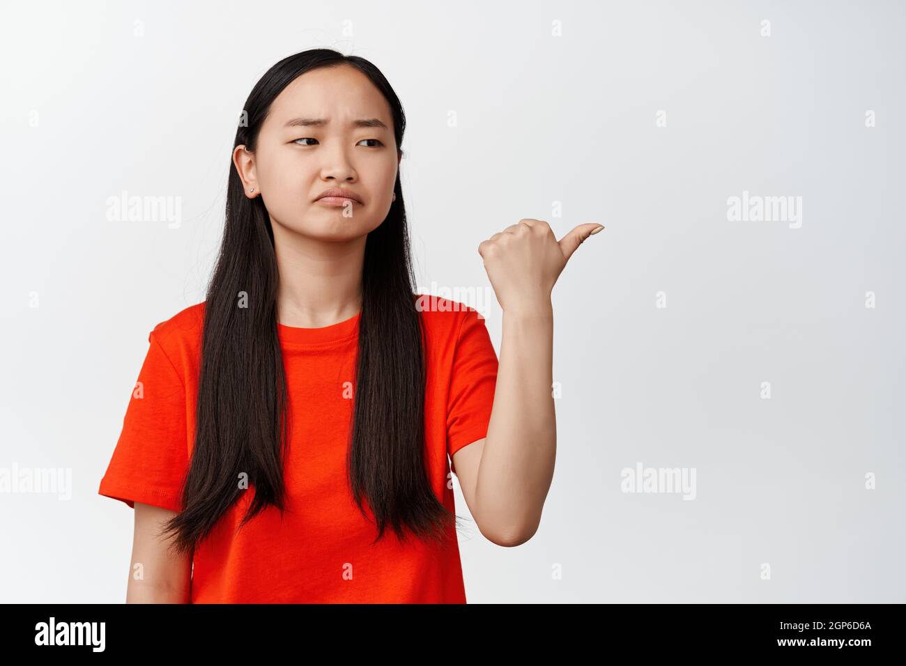 La ragazza cinese, cupa, frena, punta e guarda a destra con delusione, si sente frustrato su sfondo bianco Foto Stock