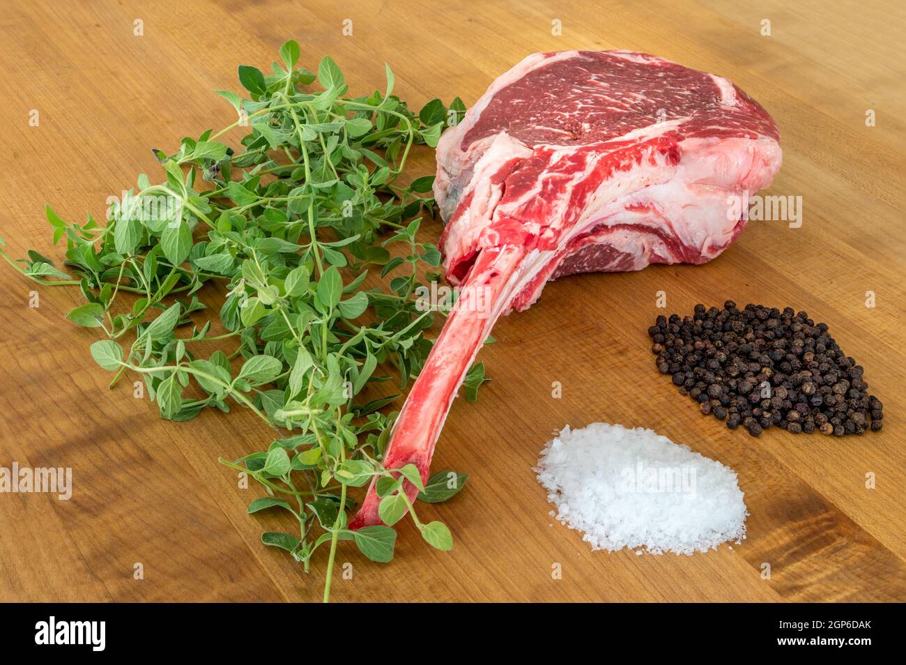 Bistecca di angus Tomahawk cruda su tavola di legno con sale, pepe, origano e un coltello Foto Stock