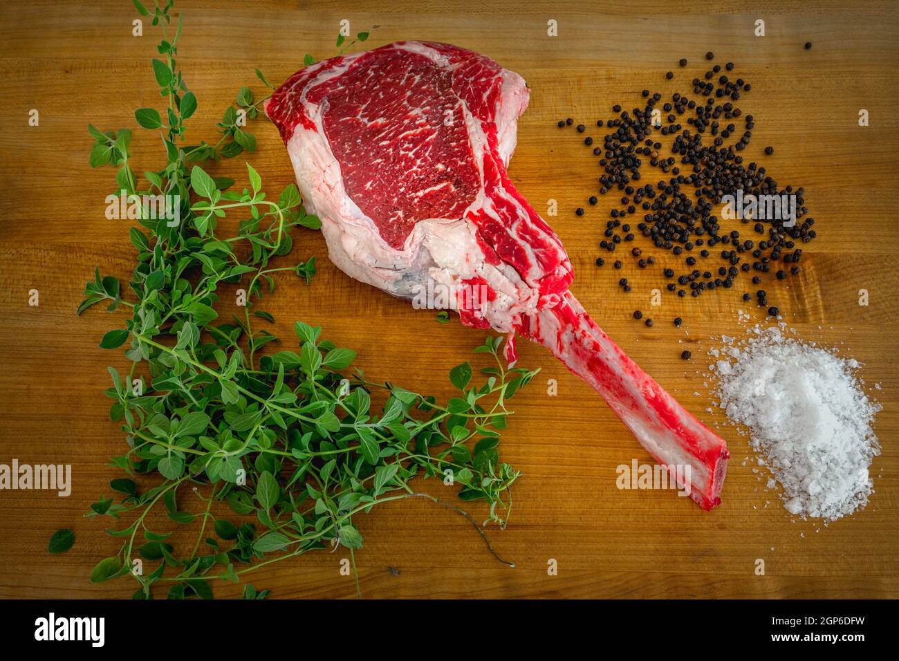 Bistecca di angus Tomahawk cruda su tavola di legno con sale, pepe, origano e un coltello Foto Stock
