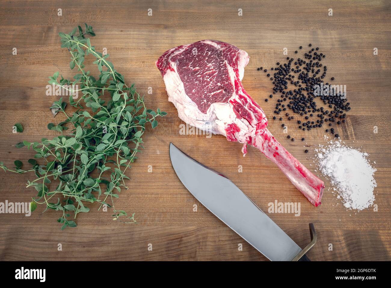 Bistecca di angus Tomahawk cruda su tavola di legno con sale, pepe, origano e un coltello Foto Stock