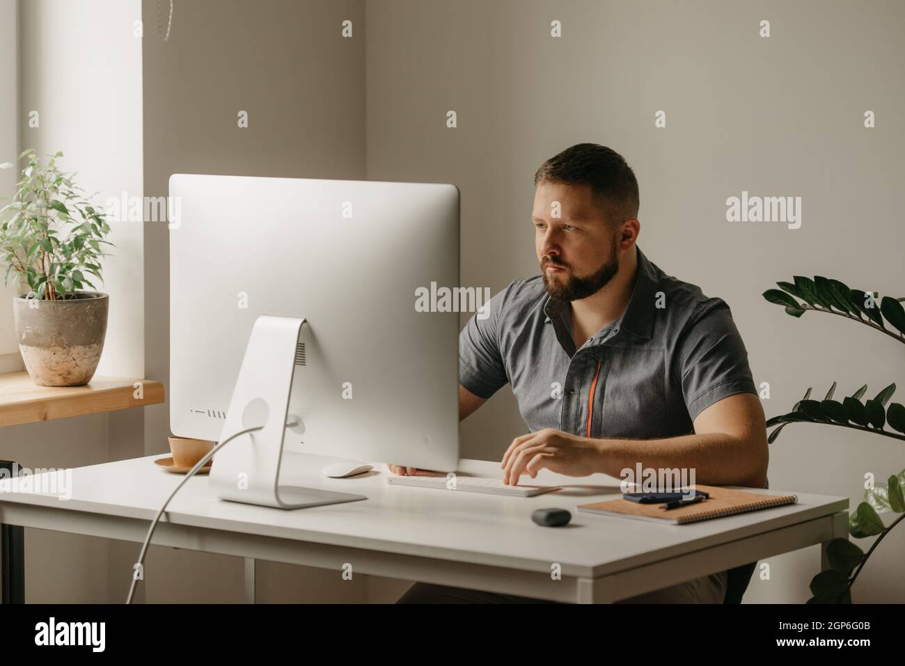 Un uomo lavora in remoto su un computer desktop. Un ragazzo con una barba sta digitando durante il rapporto di un collega a una videoconferenza a casa. Un insegnante è Foto Stock