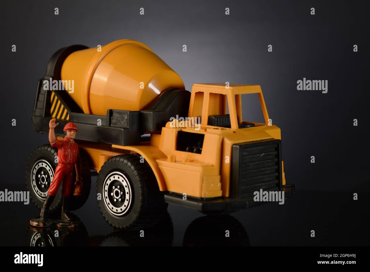 Un mixer giocattolo per cemento e un uomo da lavoro in miniatura che ondola su uno sfondo scuro e sfumato. Foto Stock