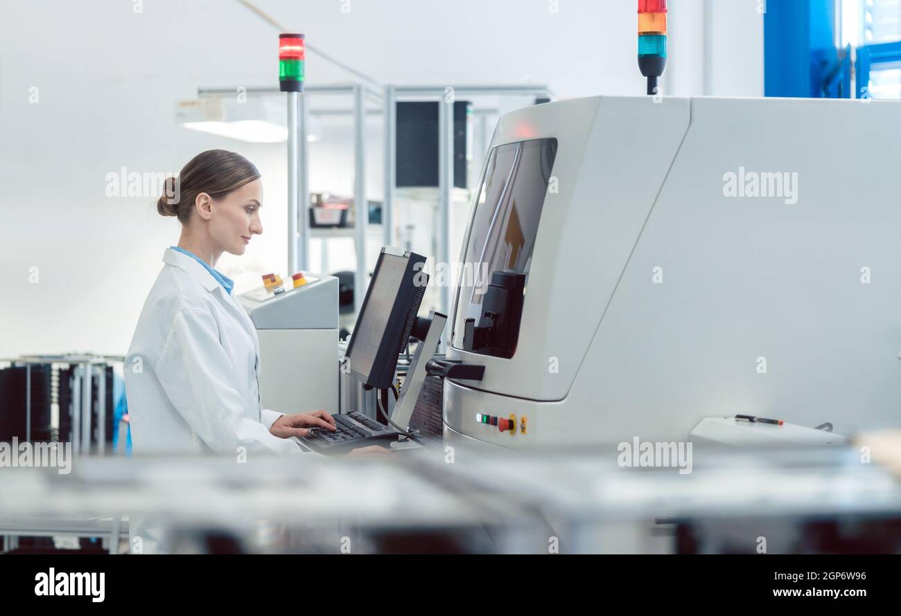 Lavoratrice in una fabbrica moderna che utilizza una saldatrice per linea di produzione elettronica Foto Stock