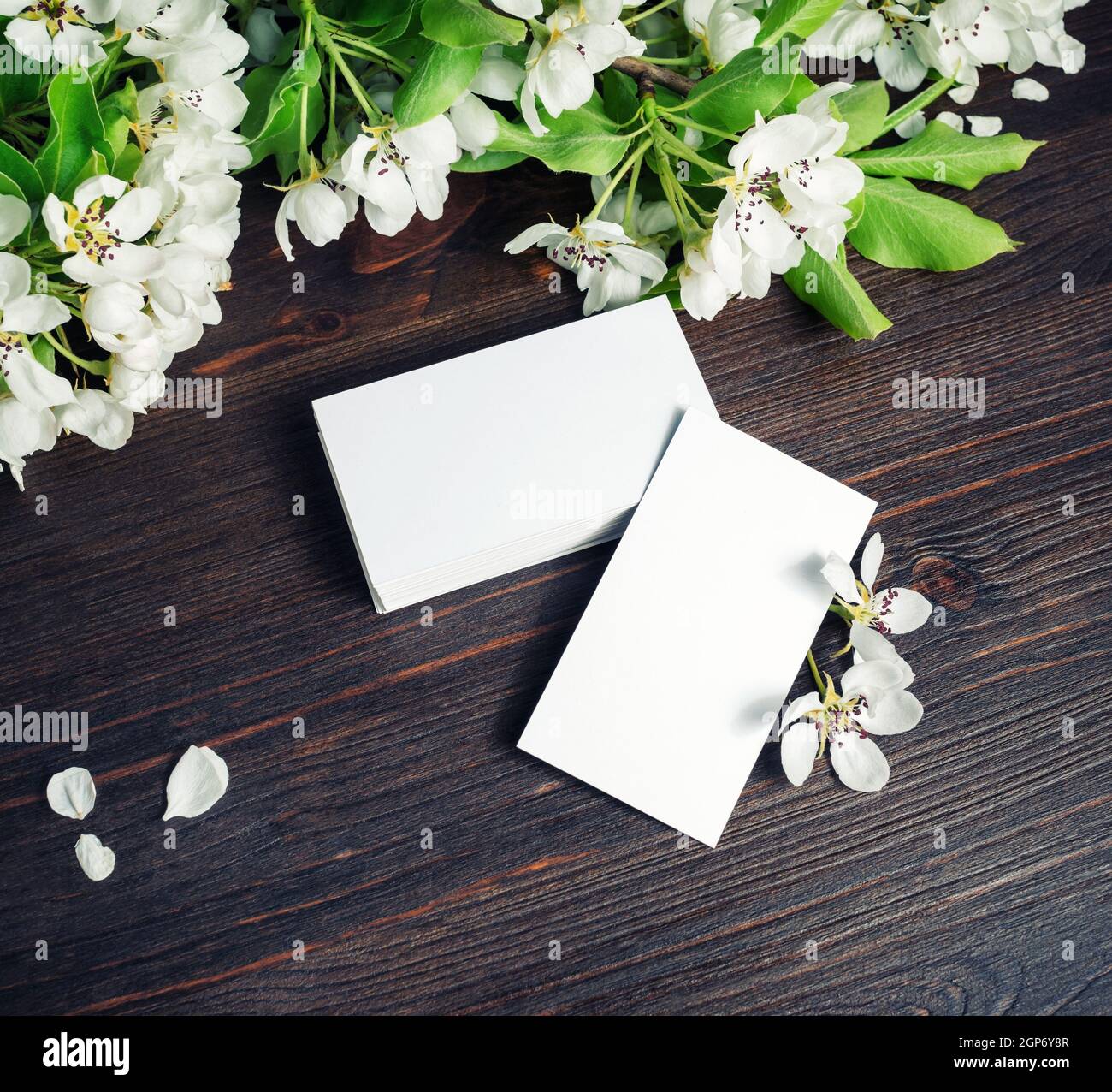 Biglietti da visita vuoti e fiori su sfondo tavola in legno. Modello per ID. Foto Stock