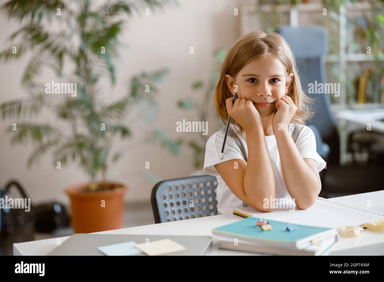 La bambina scrive in taccuino che fa i compiti alla scrivania nella stanza luminosa Foto Stock