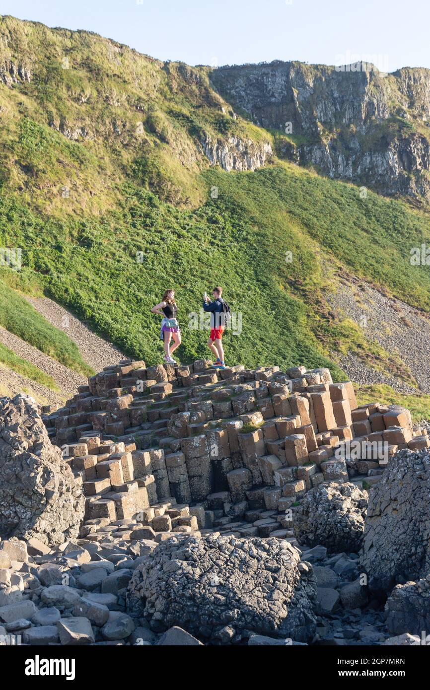 Giovane coppia in piedi su colonne di basalto, il Selciato del gigante, Causeway Coast, vicino a Bushmills, County Antrim, Irlanda del Nord, Regno Unito Foto Stock