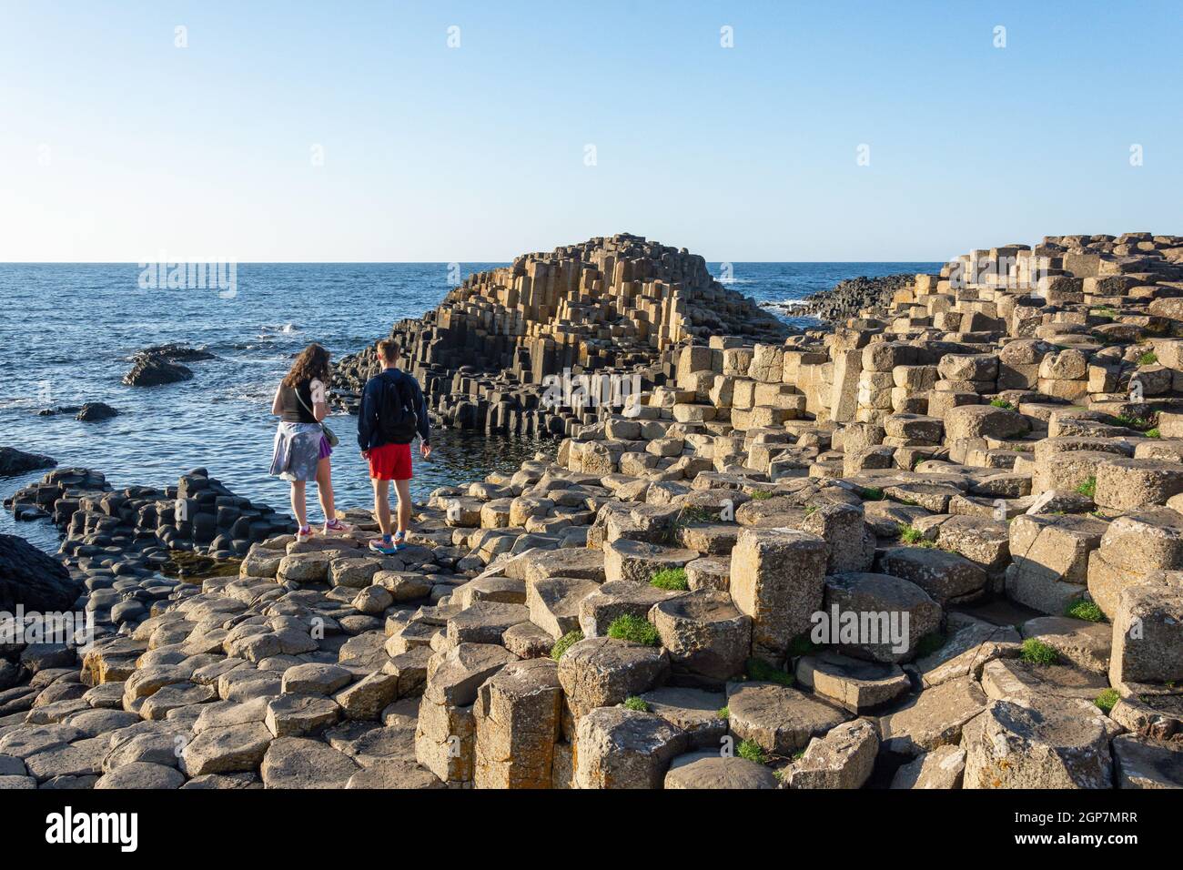 Giovane coppia in piedi su colonne di basalto, il Selciato del gigante, Causeway Coast, vicino a Bushmills, County Antrim, Irlanda del Nord, Regno Unito Foto Stock