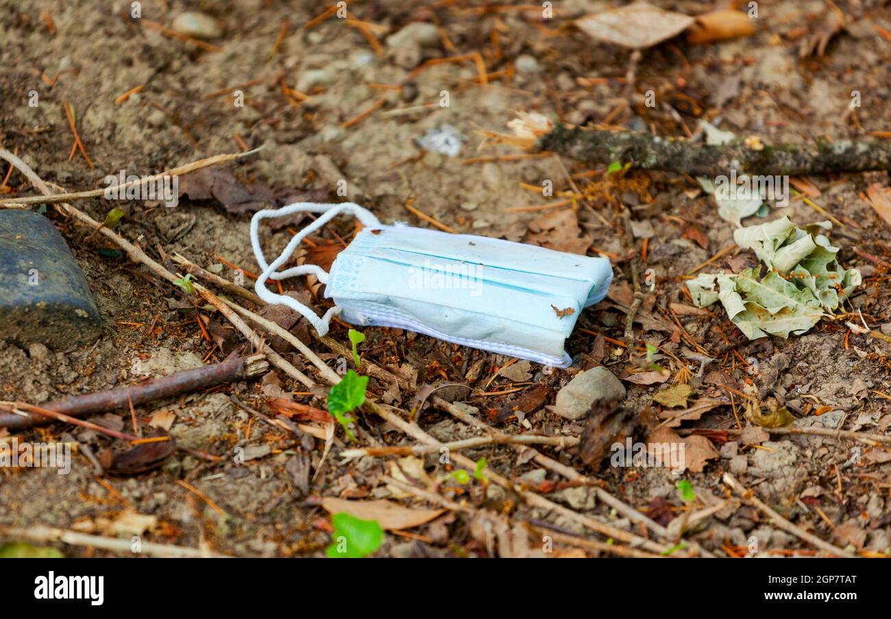 Maschera chirurgica facciale utilizzata e gettata via sul terreno nel parco. Immagine vera e autentica di una maschera sporca. Gesto incivilizzato e aumenterà t Foto Stock