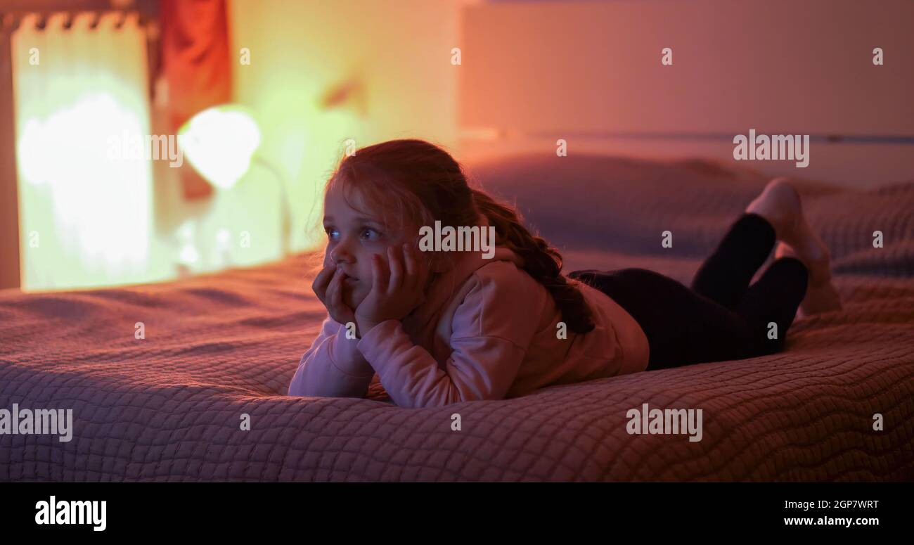 Bambina che guarda la tv in camera da letto. Luce naturale con il bagliore del display LCD. Luci basse e autentico momento della vita. Foto Stock