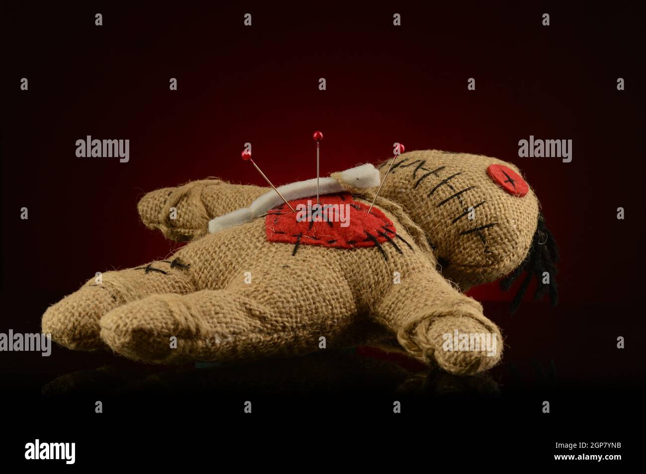 Alcuni spilli sono bloccati all'interno del cuore di una bambola voodoo su  sfondo nero e rosso scuro Foto stock - Alamy