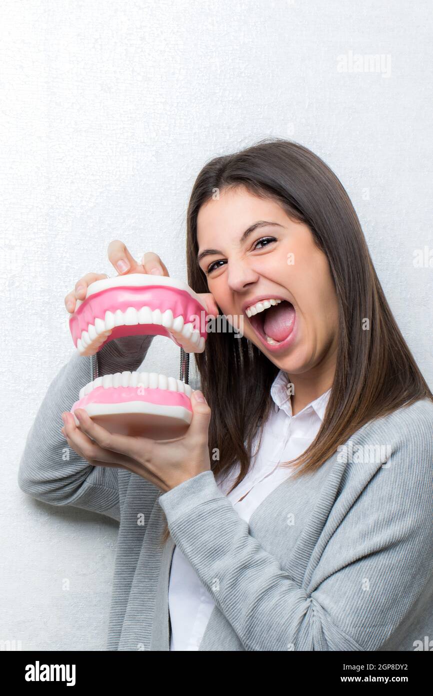 Close up divertente ritratto di attraente ragazza giovane azienda sovradimensionata denti umani protesi.donna con la bocca aperta contro la luce sullo sfondo a trama. Foto Stock