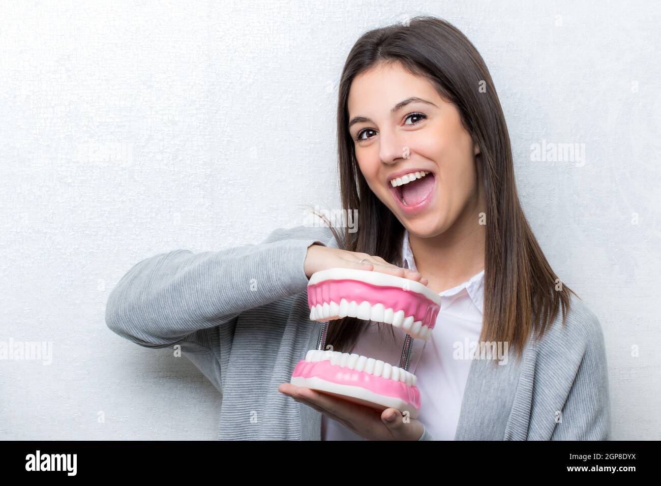 Close up ritratto di attraente ragazza giovane azienda sovradimensionata denti umani protesi.donna con la bocca aperta espressione facciale contro luce perfetta bac Foto Stock