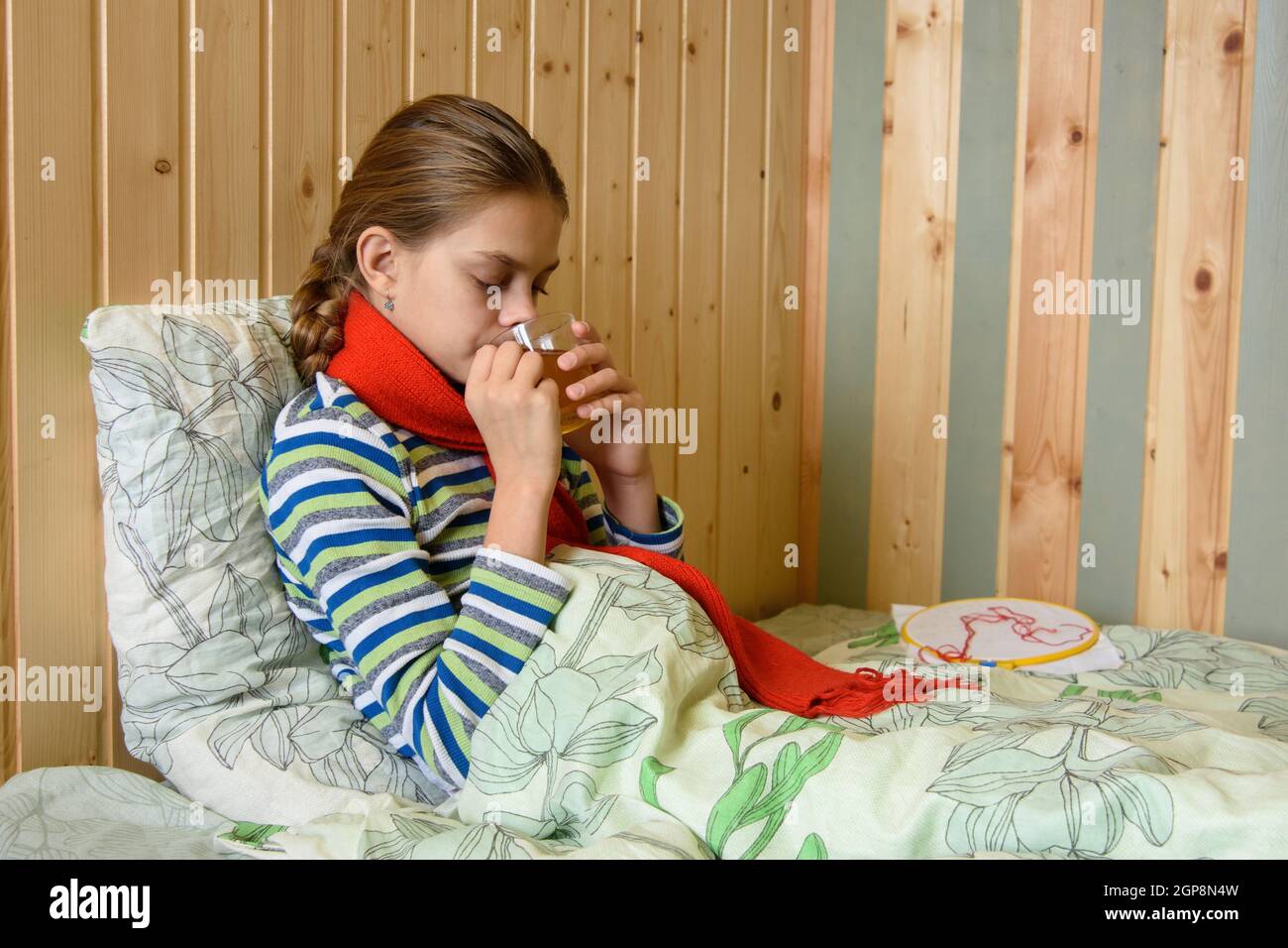 Ragazza malata che beve il tè mentre si siede a letto Foto Stock