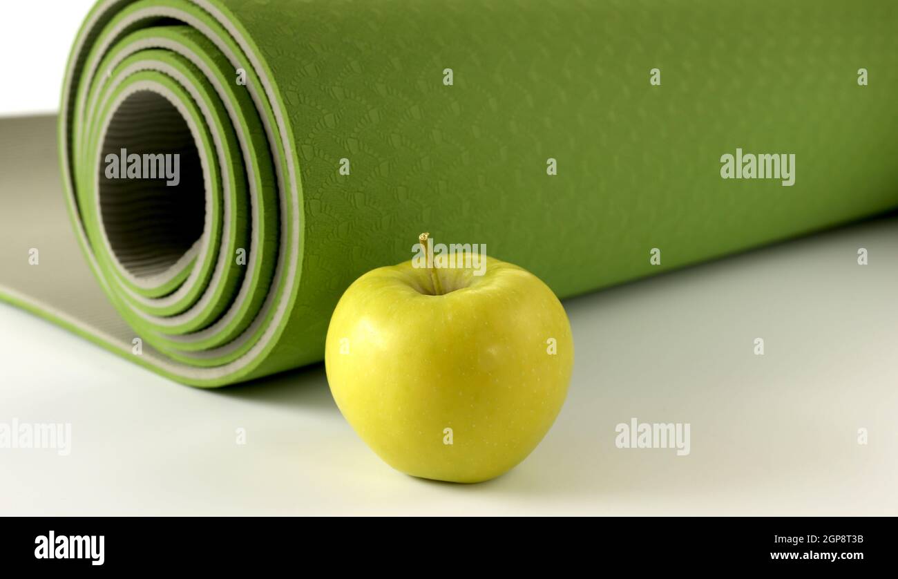 Yoga fitness, stile di vita. Yoga rotolato verde mat e mela verde su sfondo bianco. Posiziona per il testo. Stile di vita sano, fitness, concetto sportivo Foto Stock