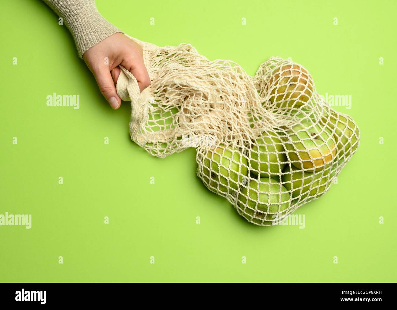 borsa in tessuto beige a mano con mele verdi su sfondo verde, il concetto di oggetti riutilizzabili, zero rifiuti Foto Stock
