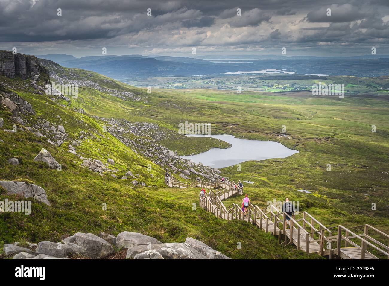 Le persone che si godono una passeggiata su ripide scale di legno passerella sulla riva del Monte Cuilcagh con una vista sul lago e la valle sottostante, Irlanda del Nord Foto Stock