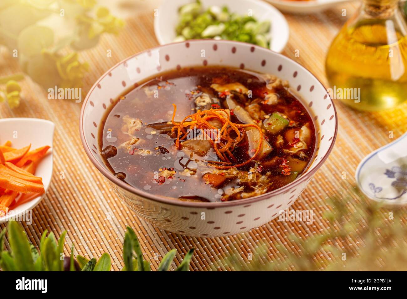 Deliziosa zuppa cinese tradizionale in ciotola su tovaglia di bambù Foto Stock