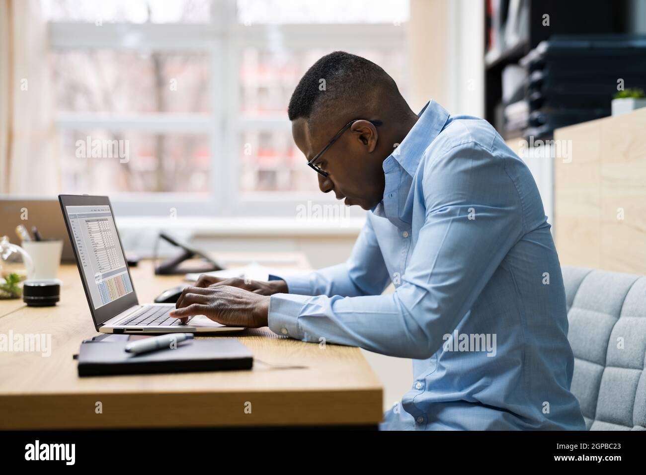 Uomo africano cattiva postura di lavoro digitando alla scrivania Foto Stock