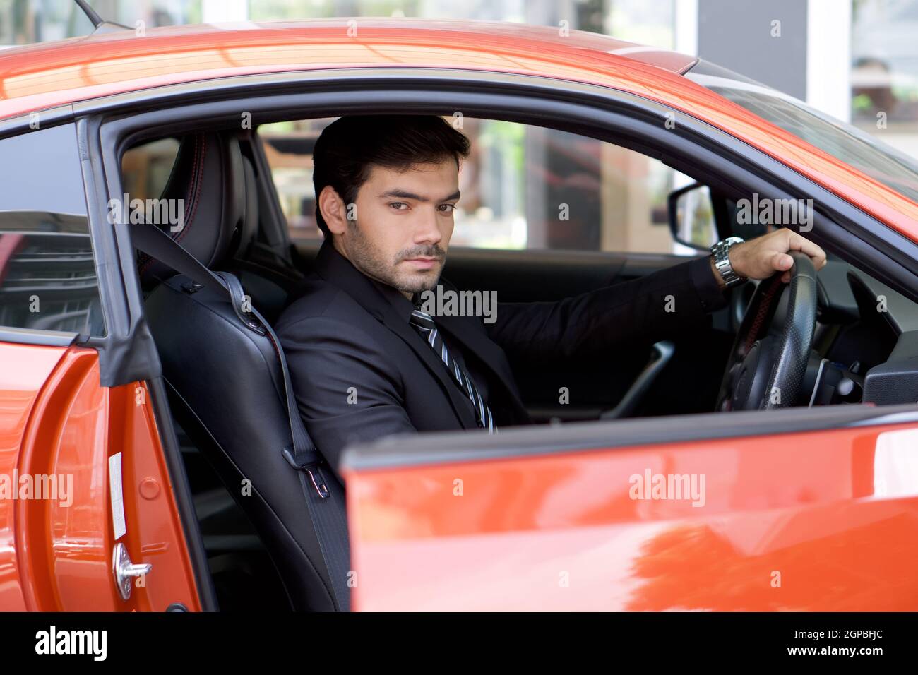 Giovane uomo d'affari in una tuta nera aprire la porta dell'auto sportiva mentre si tiene la ruota. Foto Stock