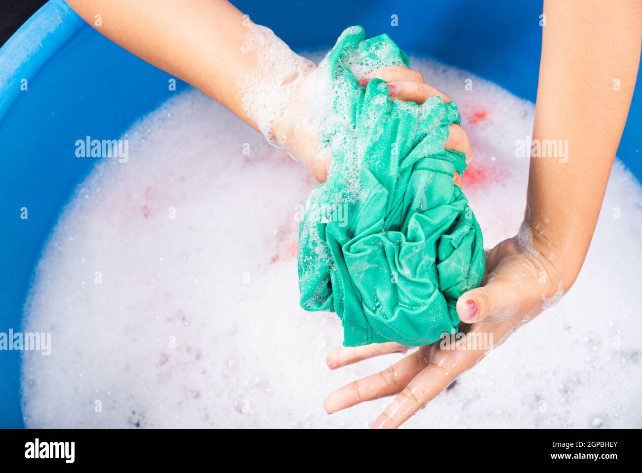 Closeup giovane donna asiatica uso mani lavare abiti colore in bacino. La donna strizzava il panno di tessuto bagnato con detergente e ha bolle di sapone in wate Foto Stock