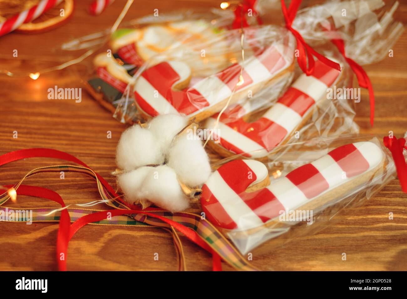 Pan di zenzero in forma di barrette di zucchero su tavola di legno. Biscotti con glassa rossa e bianca a strisce. Dolci natalizi in sacchetti con nastri. Foto Stock