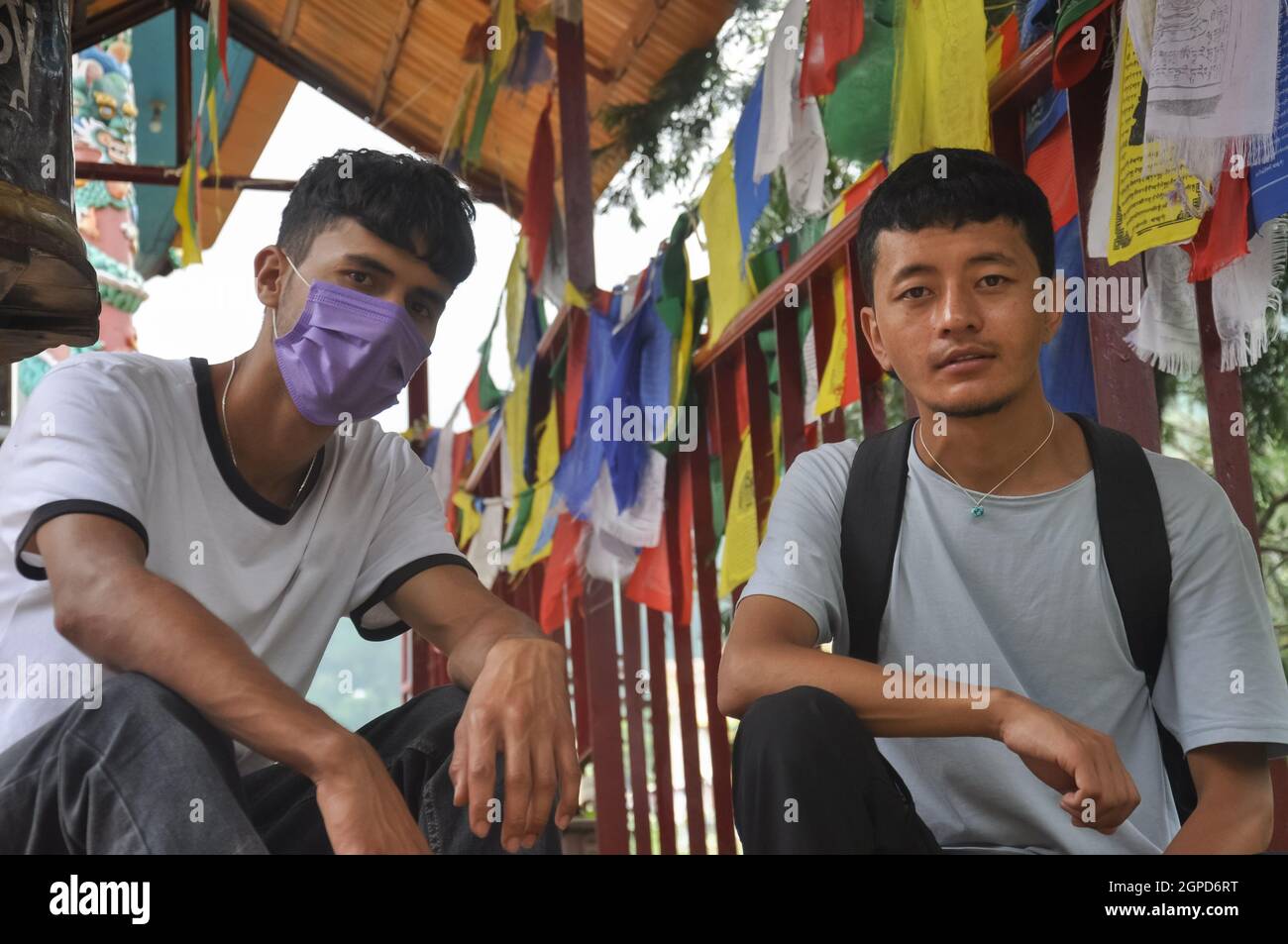 Due amici maschi che guardano la macchina fotografica con seduta sulle scale del tempio buddista a Tso Pema durante la pandemia del convivio-19 Foto Stock