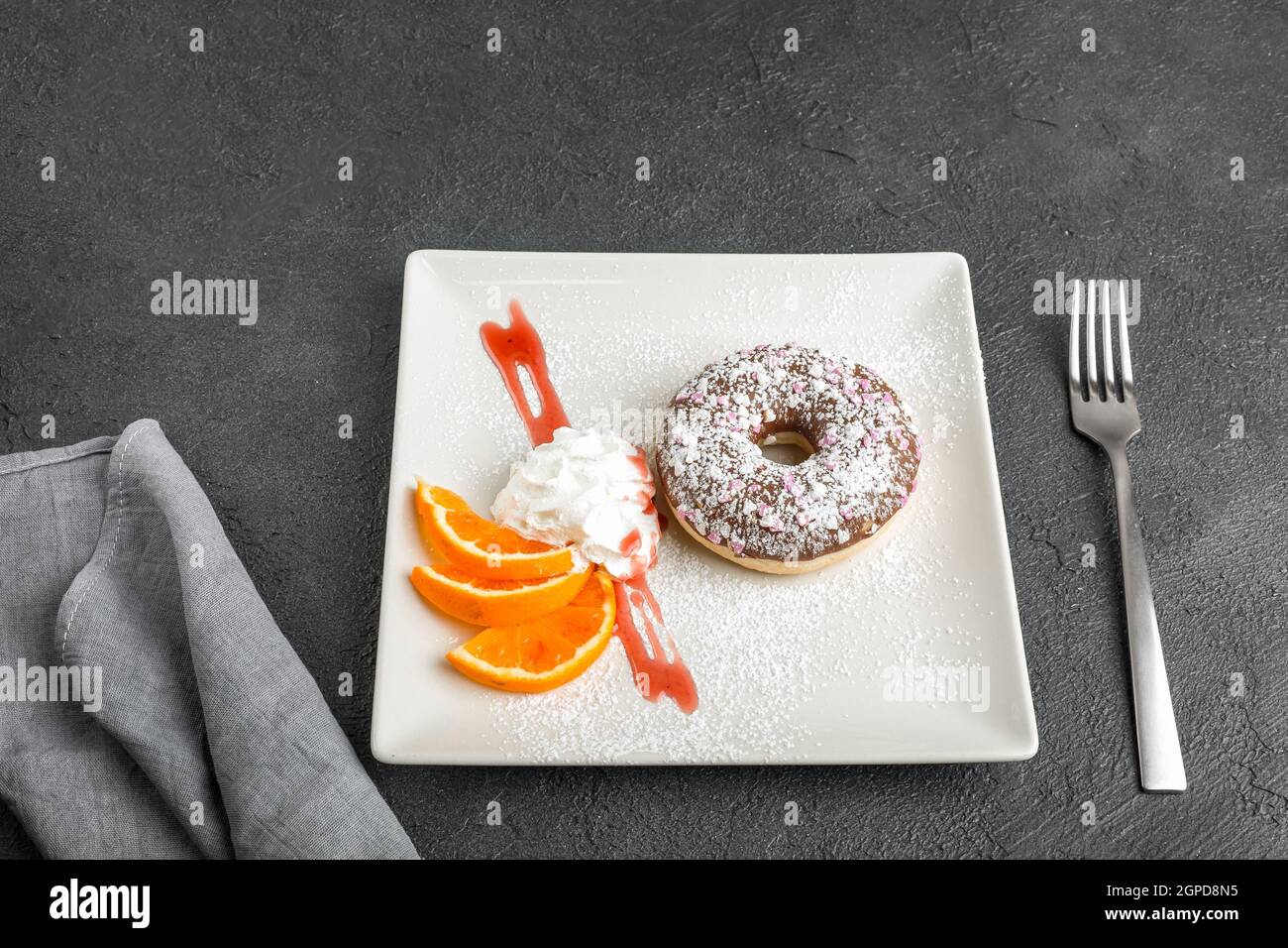 Ciambella decorata con cuori e zucchero in polvere. Servito su un piatto nero con fette arancioni. Concetto di menu del ristorante. Disposizione piatta. Messa a fuoco selettiva. Foto Stock