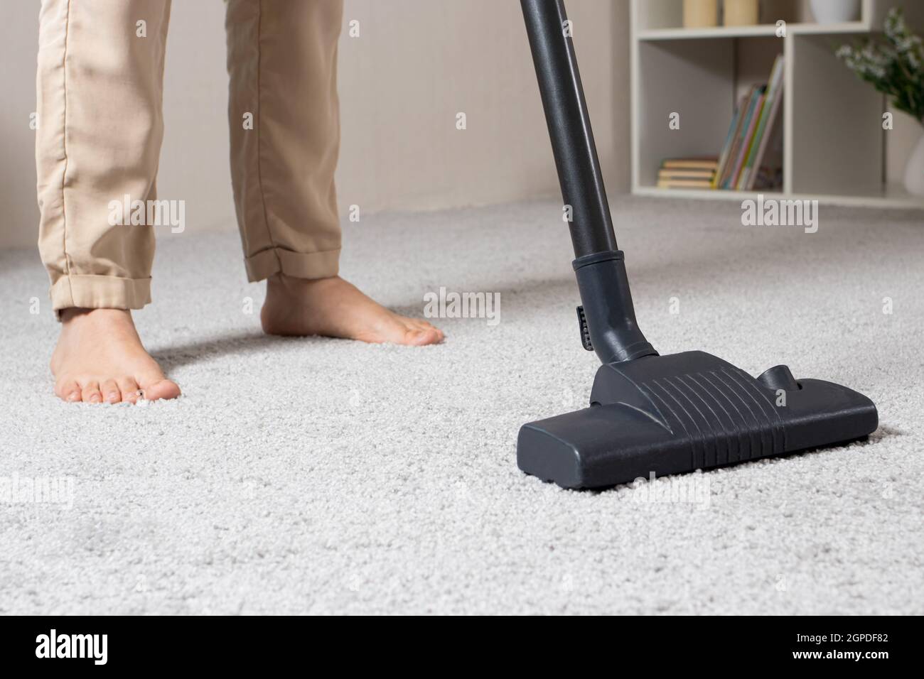 Donna che aspira il tappeto grigio con l'aspirapolvere portatile primo piano. Foto Stock