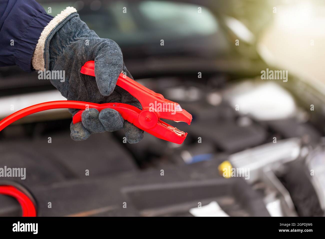 Persona che tiene il cavo rosso del ponticello vicino all'auto in primo piano. Auto che parte da vicino. Batteria per auto a carica umana con morsetti di alimentazione. Persona con energ Foto Stock