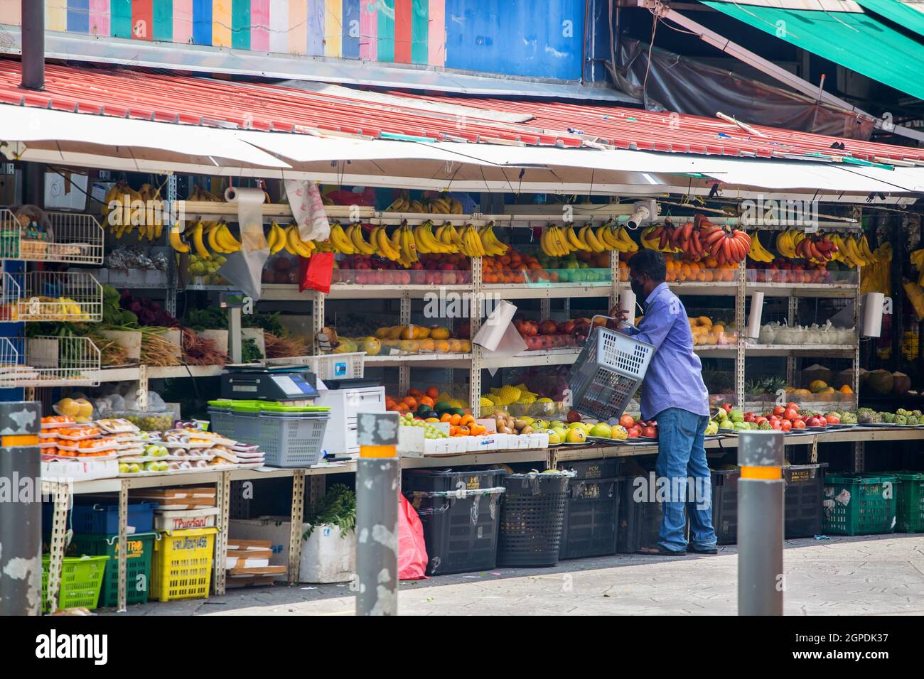 Uomo indiano con un cestino a fare shopping in un vivace chiosco di frutta all'aperto a Little India, Singapore. Cattura la vita quotidiana di strada e lo stile di vita della cultura locale. Foto Stock