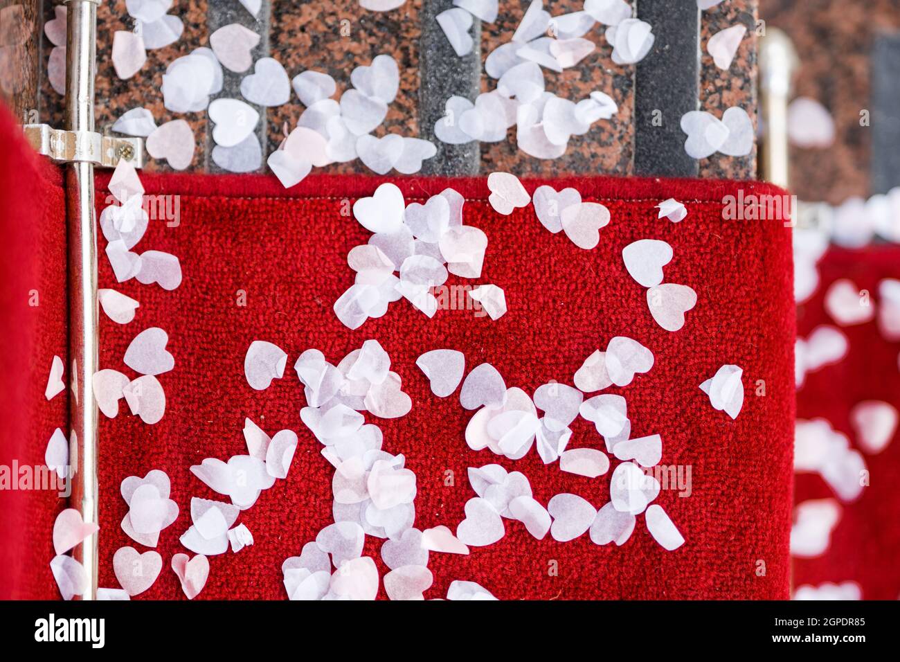 I bei confetti di nozze amano la forma del cuore scattano sul tappeto rosso dopo essere stati gettati sopra la sposa e lo sposo per celebrare la cerimonia di matrimonio. Romantico. Foto Stock