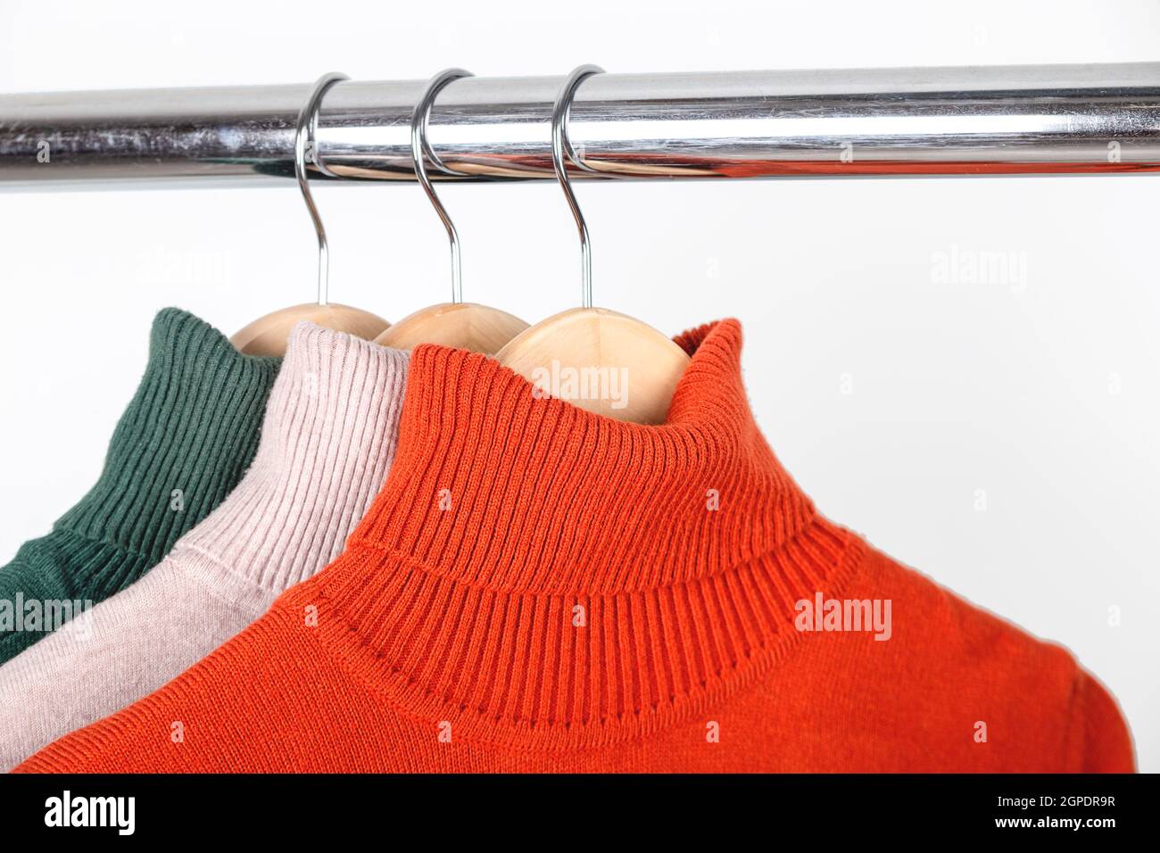 Il concetto di base di guardaroba per donna d'autunno. Maglioni di dolcevita vuoti su appendiabiti. Girocollo color ocra arancio brillante con beige e verde. Foto Stock