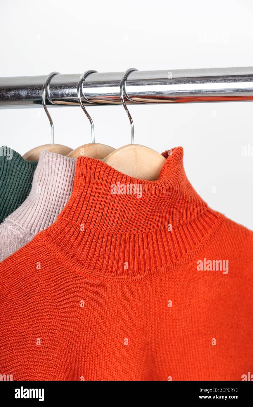 Il concetto di base di guardaroba per donna d'autunno. Maglioni di dolcevita vuoti su appendiabiti. Girocollo color ocra arancio brillante con beige e verde. Foto Stock