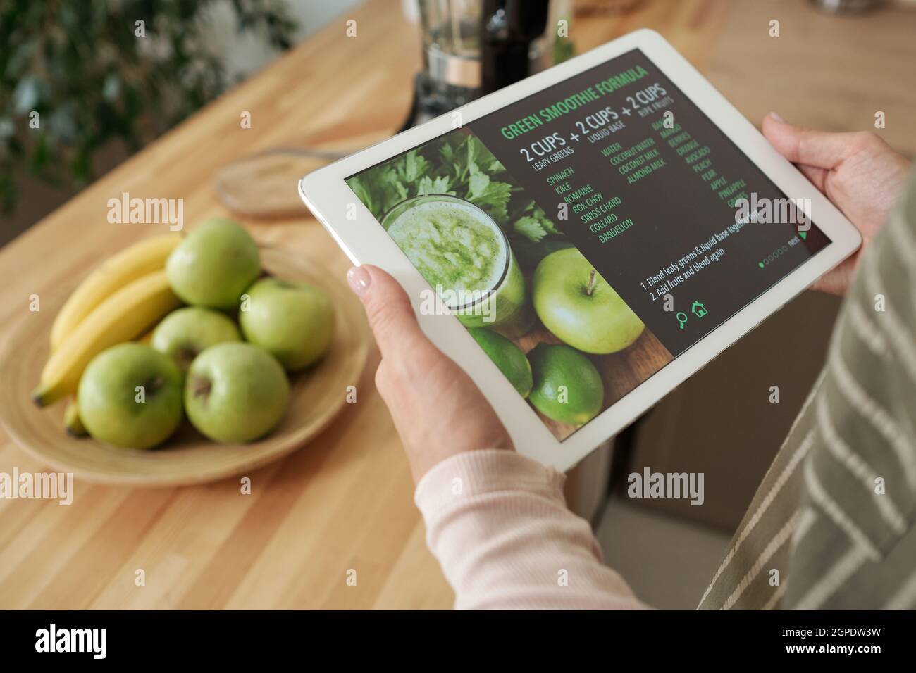 Primo piano ad angolo di una donna irriconoscibile che tiene in mano il tablet digitale leggendo la ricetta del frullato in Internet Foto Stock