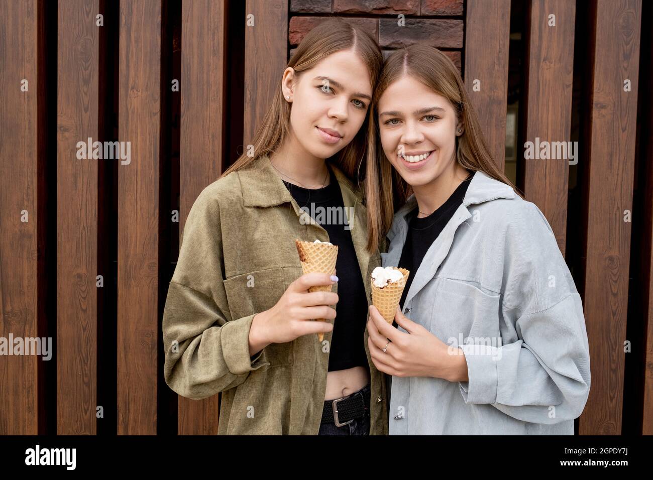 Due ragazze graziose dell'adolescenza con i coni del icecream che si levano in piedi contro l'esterno della costruzione Foto Stock
