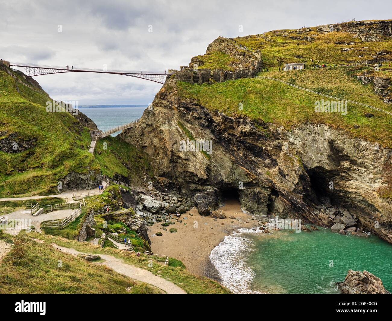 Ponte pedonale Tintagel con la Grotta di Merlin e la Cove Tintagel in primo piano. Foto Stock