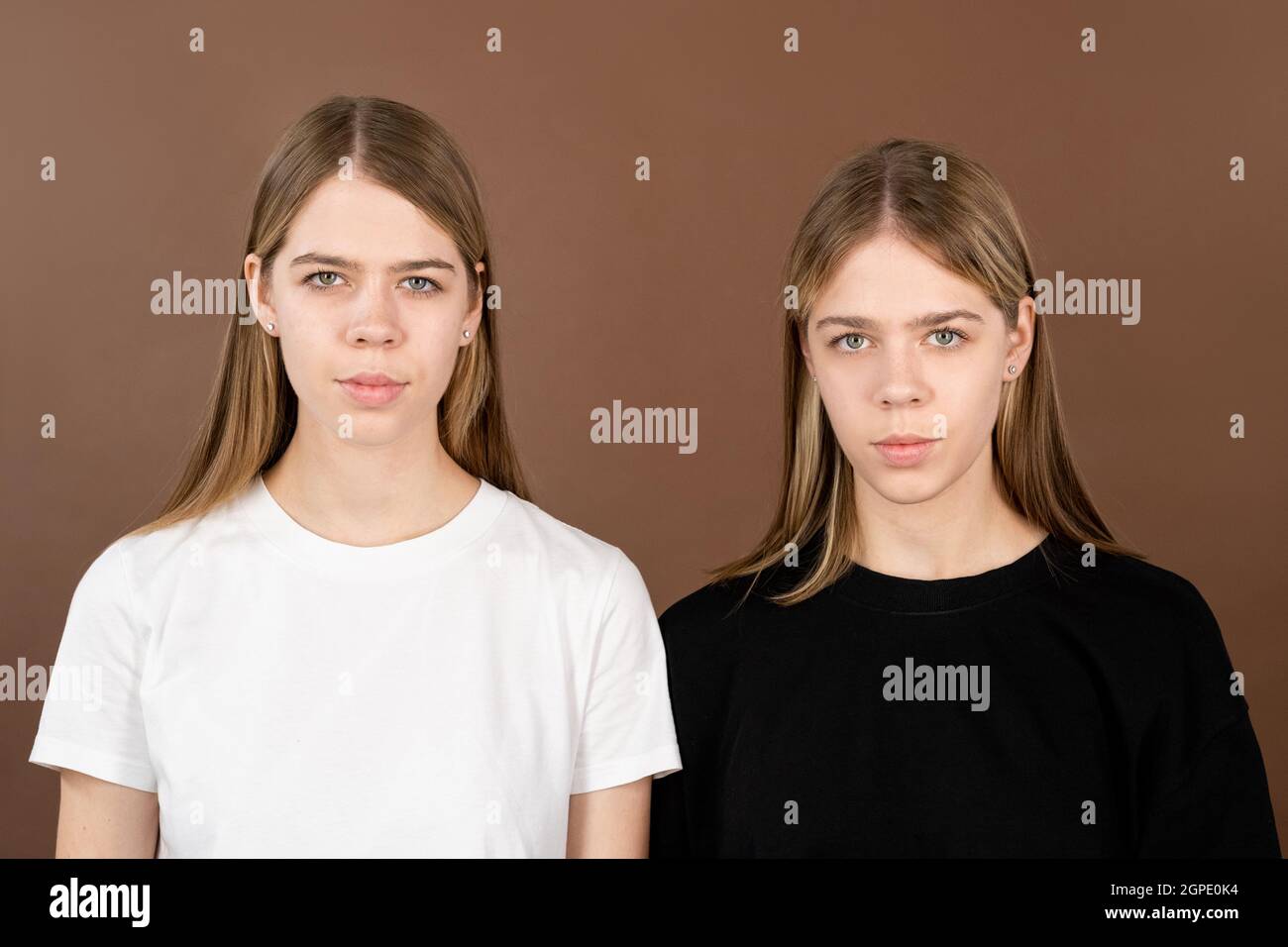 Due ragazze serie carine in t-shirt guardando la macchina fotografica su sfondo marrone Foto Stock